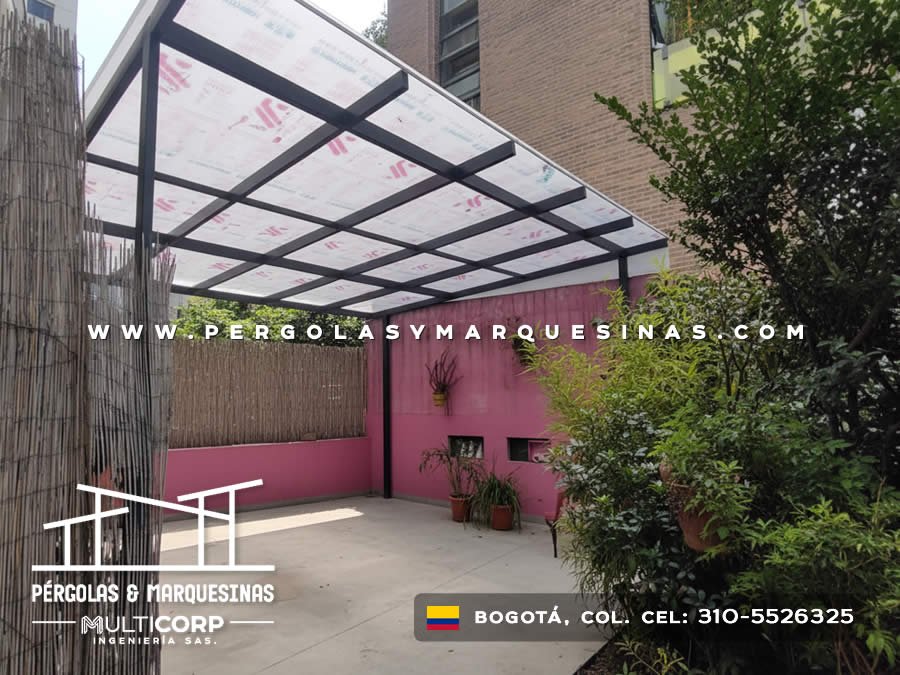 Pérgola metálica negra policarbonato patio muro rosa vegetación macetas piso concreto en Bogotá, Colombia. Multicorp Ingeniería SAS.