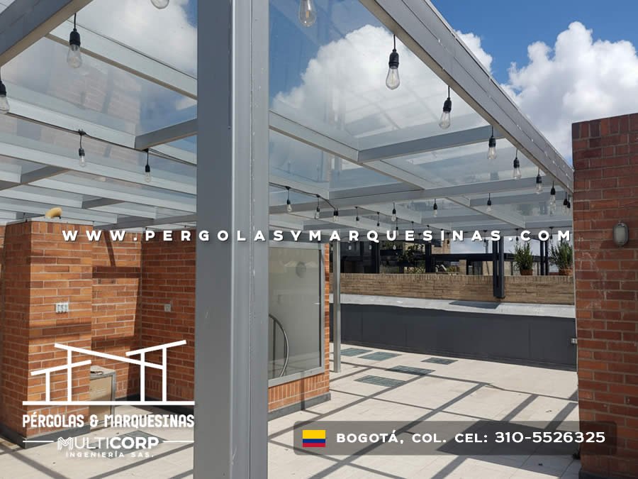 Pergola con techo de vidrio templado estructura metalica blanca y luces colgantes en terraza urbana en Bogotá, Colombia. Multicorp Ingeniería SAS.