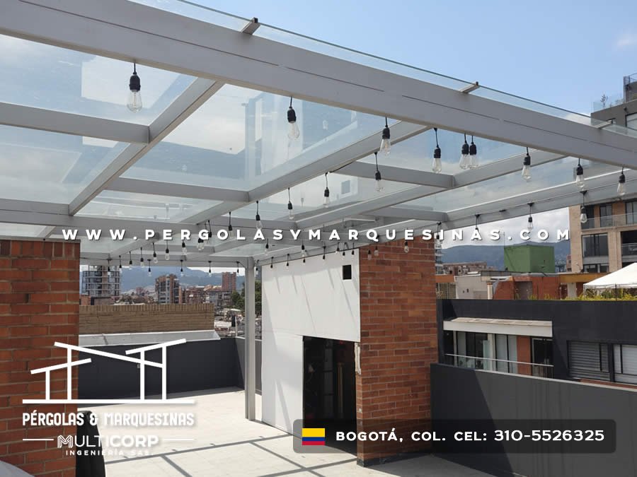 Cubierta de vidrio templado con perfiles metalicos blancos y luces decorativas en terraza de edificio urbano en Bogotá, Colombia. Multicorp Ingeniería SAS.