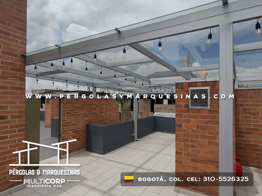 Pergola metalica con techo de vidrio templado y luces colgantes en terraza con muro de ladrillo en Bogotá, Colombia. Multicorp Ingeniería SAS.