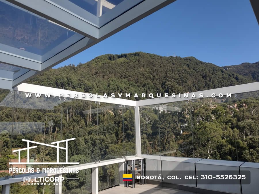 Pergola con techo de vidrio y barandilla de vidrio en terraza con vista a montes verdes en Bogotá, Colombia. Multicorp Ingeniería SAS.