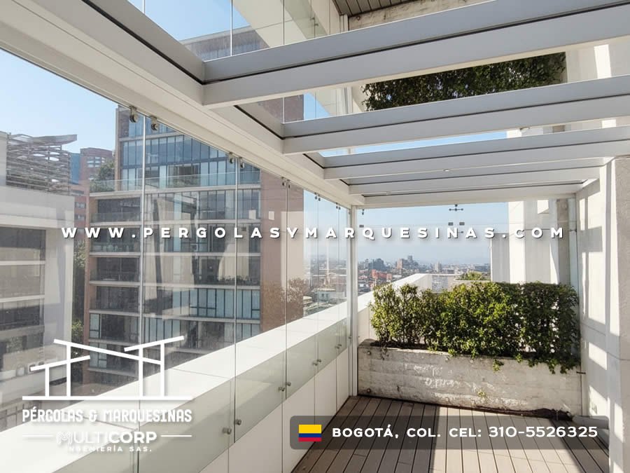 Pergola con vidrio templado cerramiento lateral y jardineras en terraza urbana con vista a torres en Bogotá, Colombia. Multicorp Ingeniería SAS.