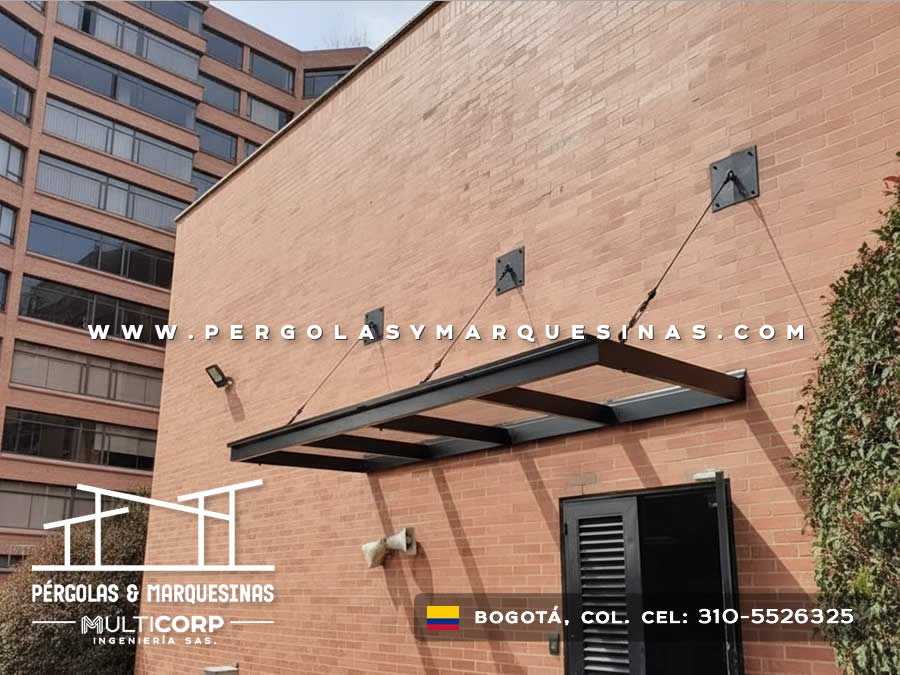 Marquesina negra suspendida por cables sobre puerta de entrada en edificio urbano de Bogotá, Colombia. Multicorp Ingeniería SAS.