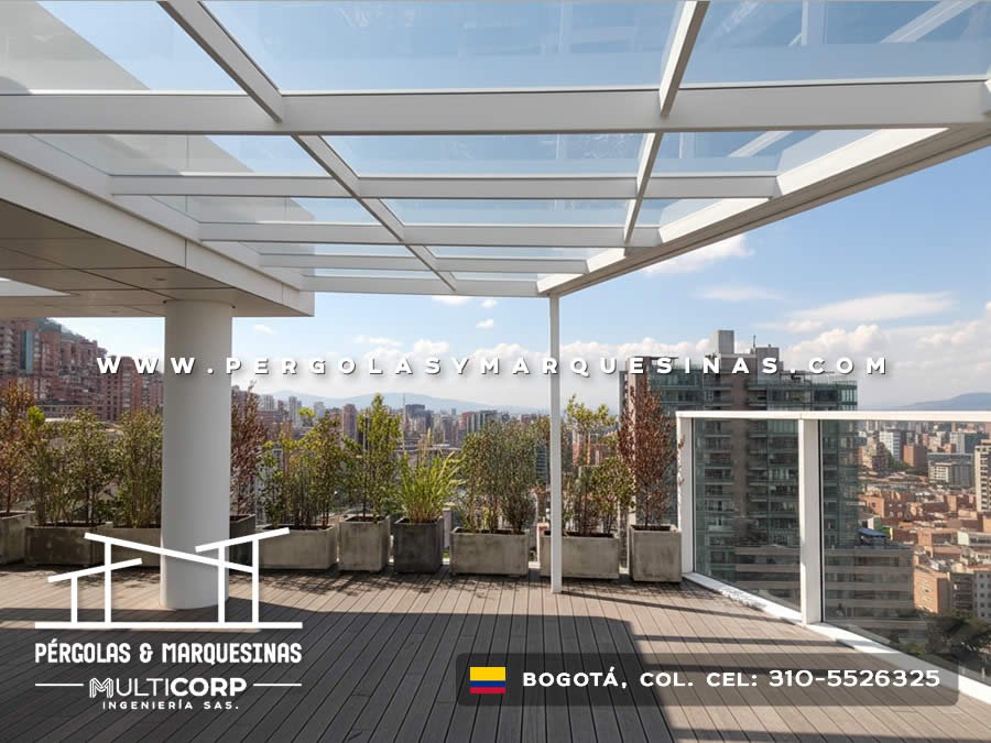 Pérgola blanca de vidrio con plantas en macetas sobre deck de madera en terraza de ático con vista urbana en Bogotá, Colombia. Multicorp Ingeniería SAS.