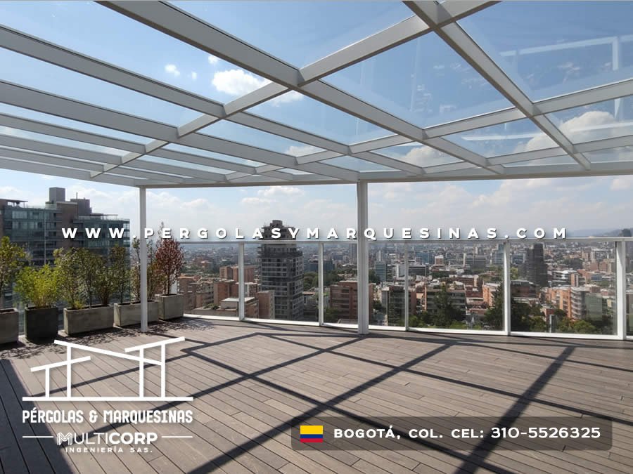 Cubierta de vidrio con estructura metálica blanca plantas en jardineras y deck de madera en terraza de ático en Bogotá, Colombia. Multicorp Ingeniería SAS.