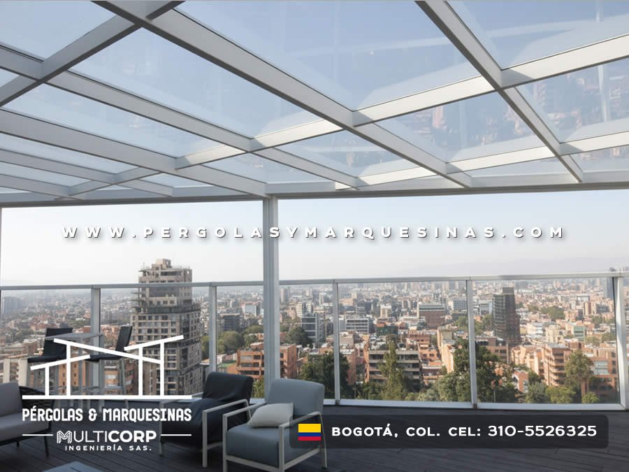 Cubierta acristalada con estructura blanca barandal transparente muebles lounge y vista urbana en terraza de ático en Bogotá, Colombia. Multicorp Ingeniería SAS.