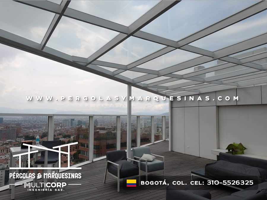Techo de vidrio con estructura metálica gris muebles lounge y cerramientos transparentes en terraza de ático en Bogotá, Colombia. Multicorp Ingeniería SAS.