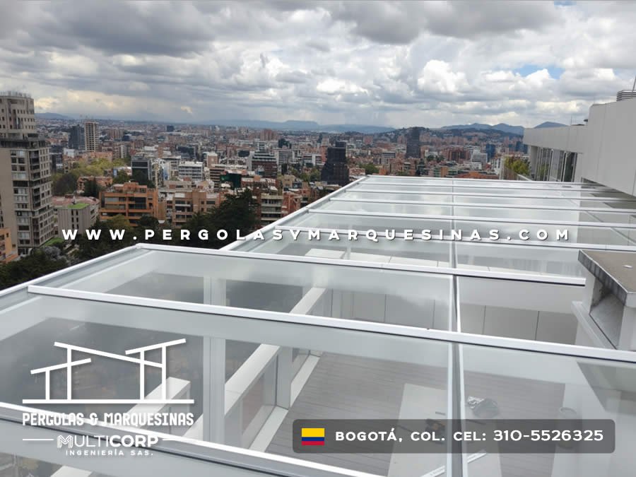 Domo de vidrio transparente con perfiles blancos sobre terraza de ático con vista a cerros en Bogotá, Colombia. Multicorp Ingeniería SAS.