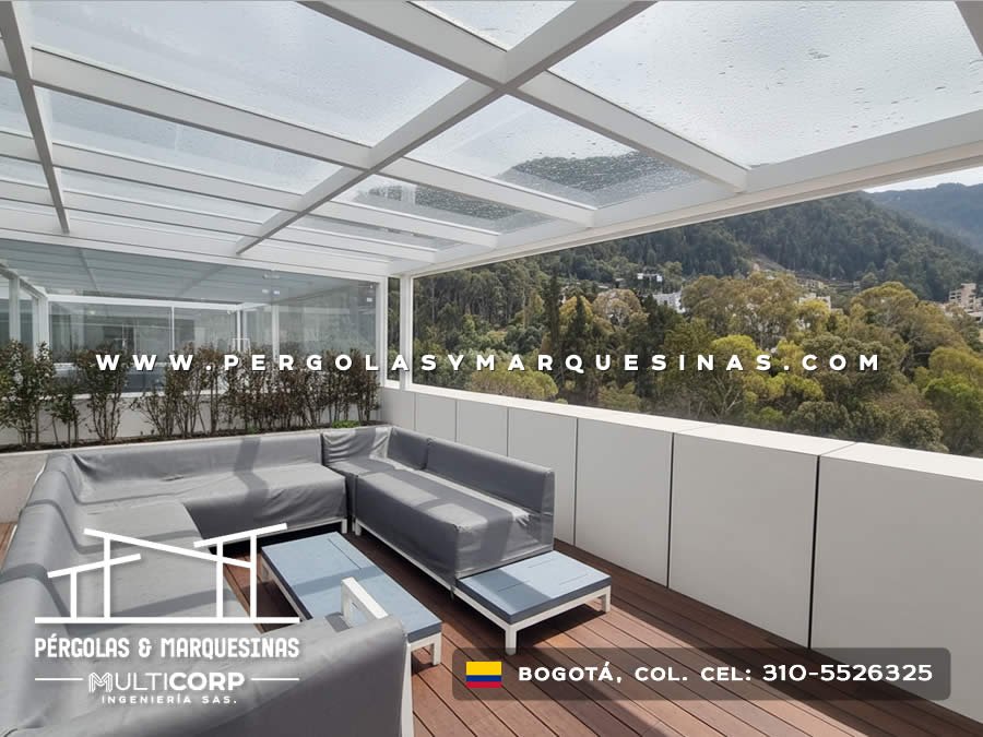 Pérgola de vidrio con estructura blanca muebles lounge plantas y deck de madera con vista a cerros en Bogotá, Colombia. Multicorp Ingeniería SAS.