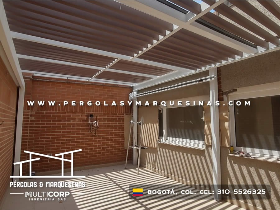 Pérgola bioclimática con listones de madera orientables estructura blanca y muro de ladrillo en Bogotá, Colombia. Multicorp Ingeniería SAS.