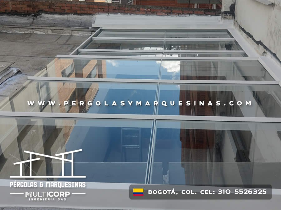 Techo de vidrio con estructura metálica blanca sobre patio interior con reflejo del exterior en Bogotá, Colombia. Multicorp Ingeniería SAS.