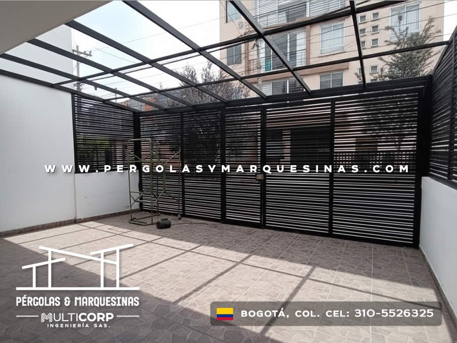 Pérgola de vidrio con estructura metálica negra y cerramiento lateral de lamas para terraza moderna en Bogotá, Colombia. Multicorp Ingeniería SAS.